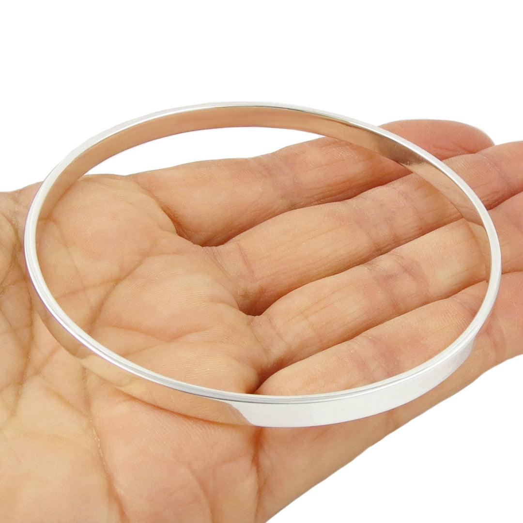 Large sterling silver circle bangle held in a person's hand.