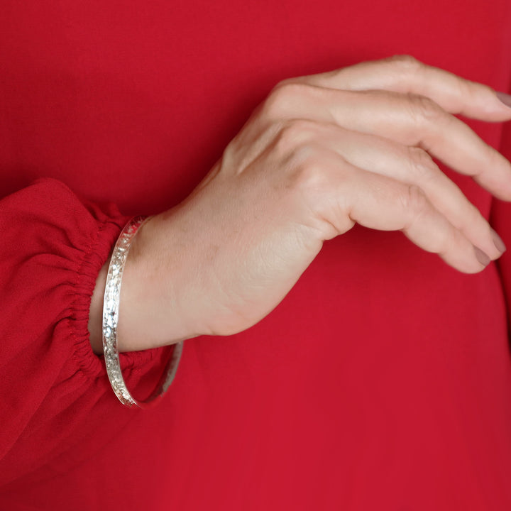 A woman wearing a red blouse and a hammered sterling silver circle bangle