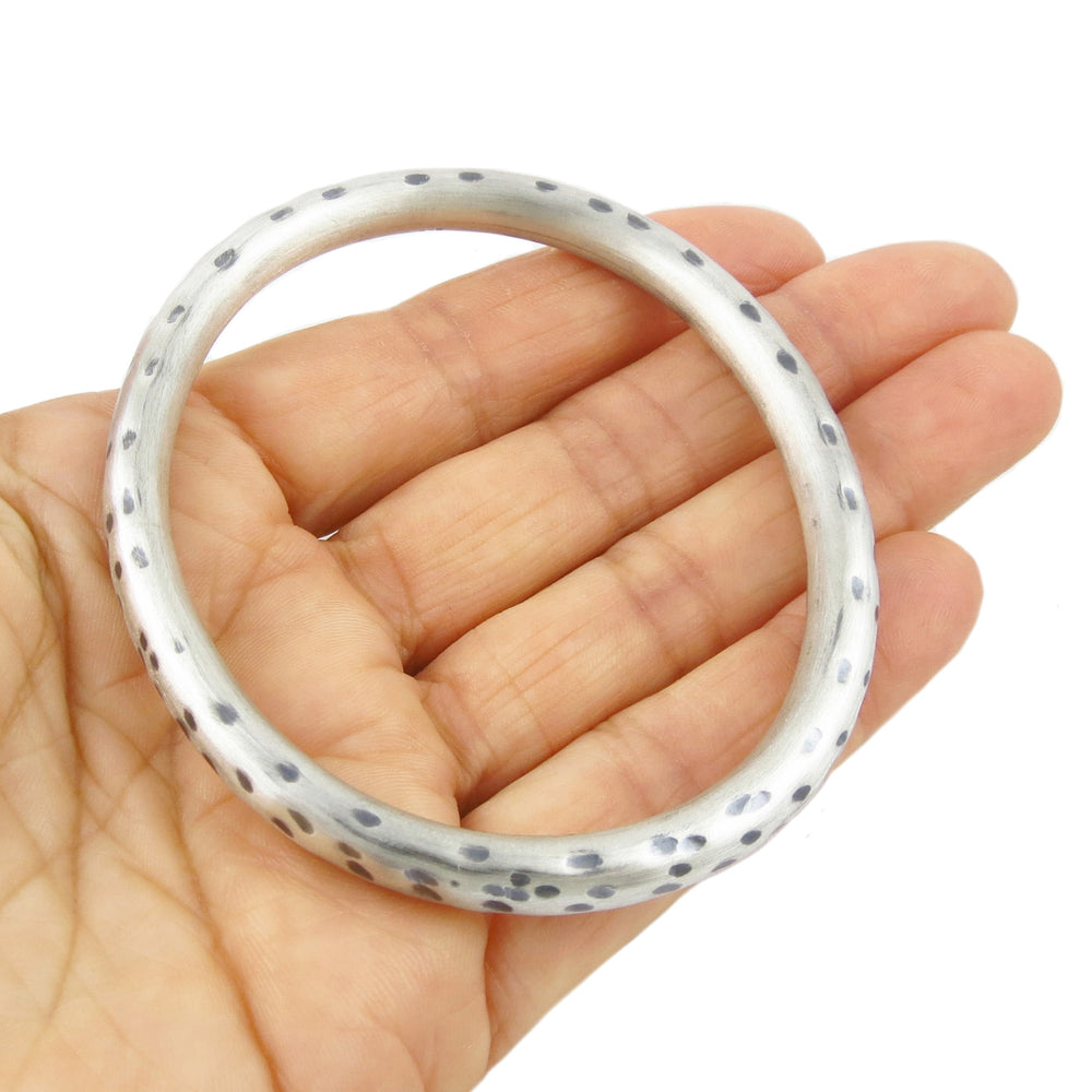 Sterling silver oval animal print bangle held in a hand on a white background