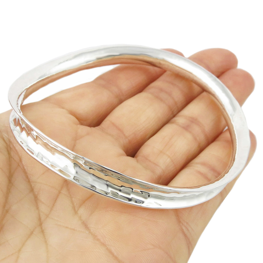 A sterling silver bracelet with a curved edge and hammered texture, held in a person's hand.