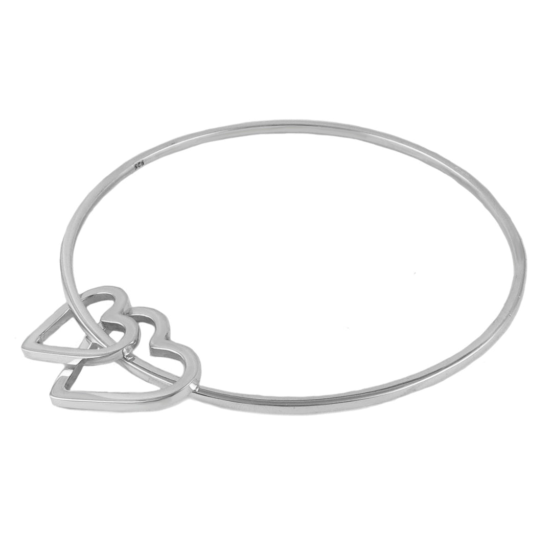 A large circle bangle with htwo heart charms on a hite background.