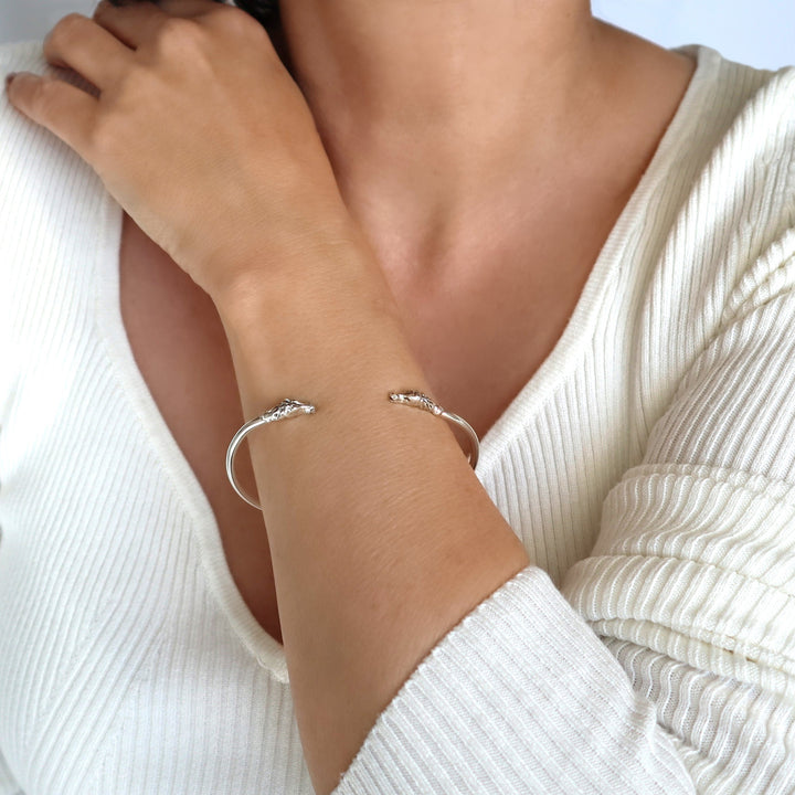 A person wearing a white sweater showcasing a sterling silver bracelet with two horse head designs at the ends.