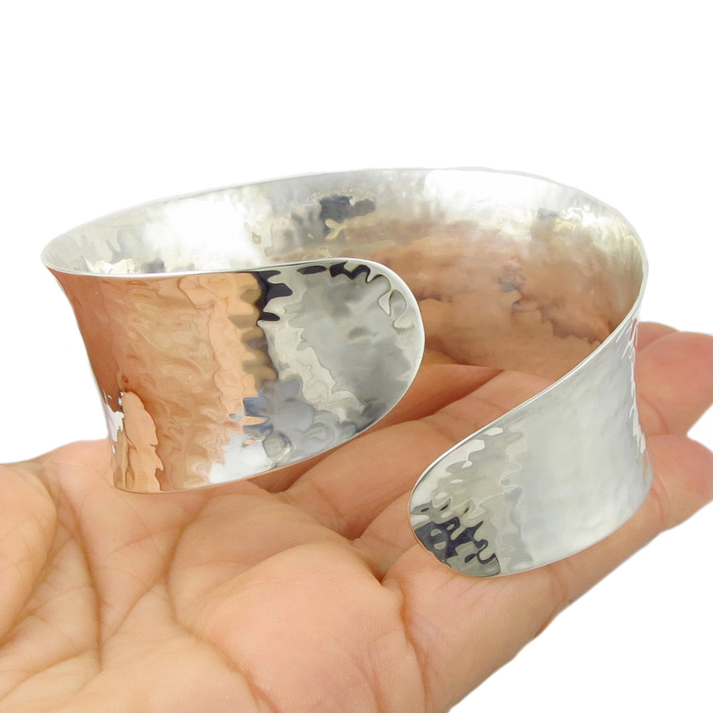 A large sterling silver overlap bracelet held in a person's hand.