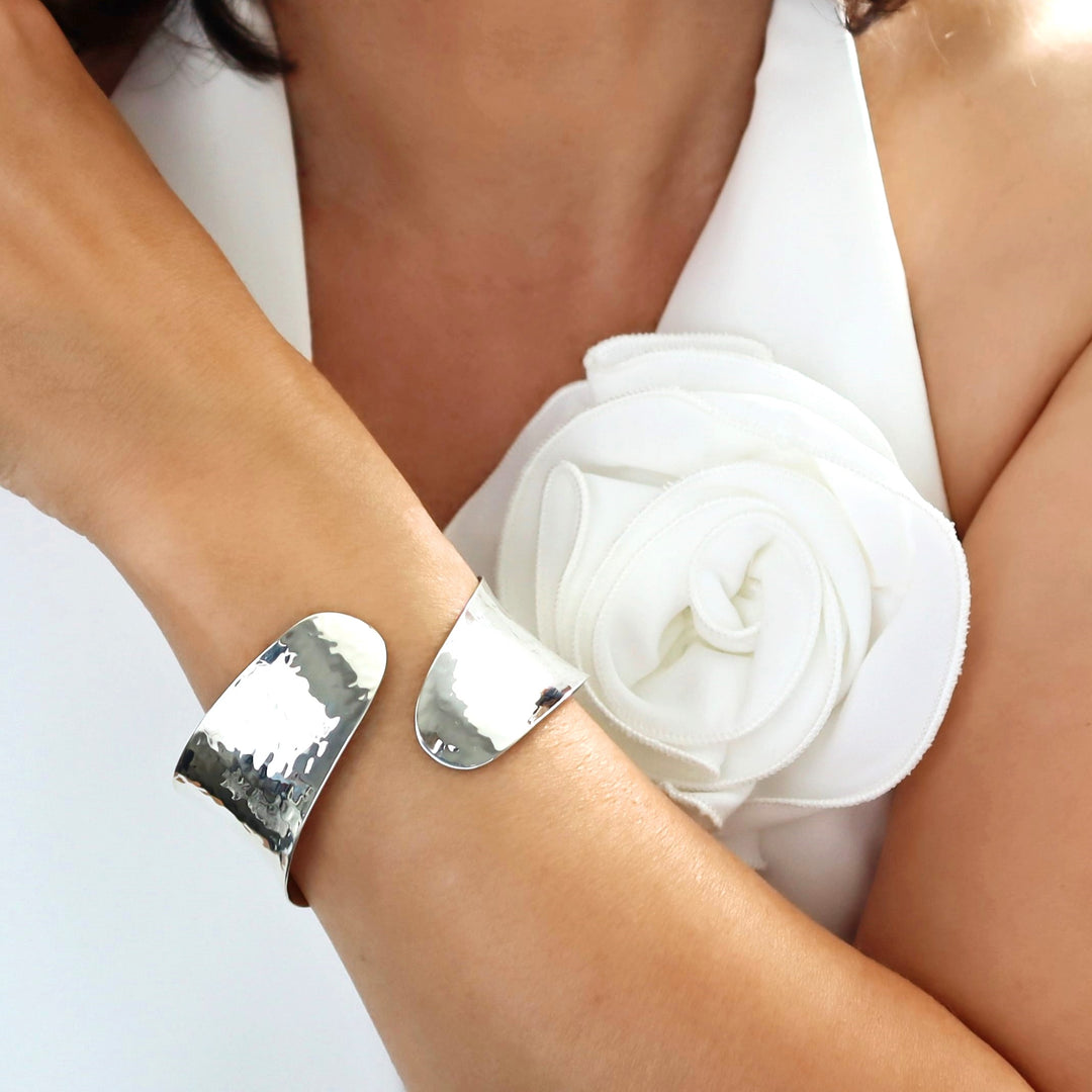 A woman wearing a sterling silver overlap bracelet with a hammered finish wearing a white waistcoat.