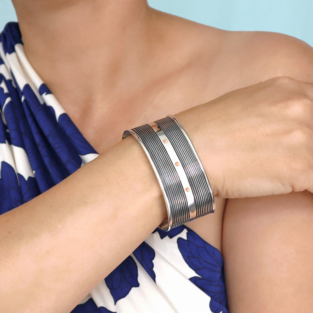 A person wearing a blue and white patterned top showcasing a Taxco silver cuff bracelet with copper dots on their wrist.