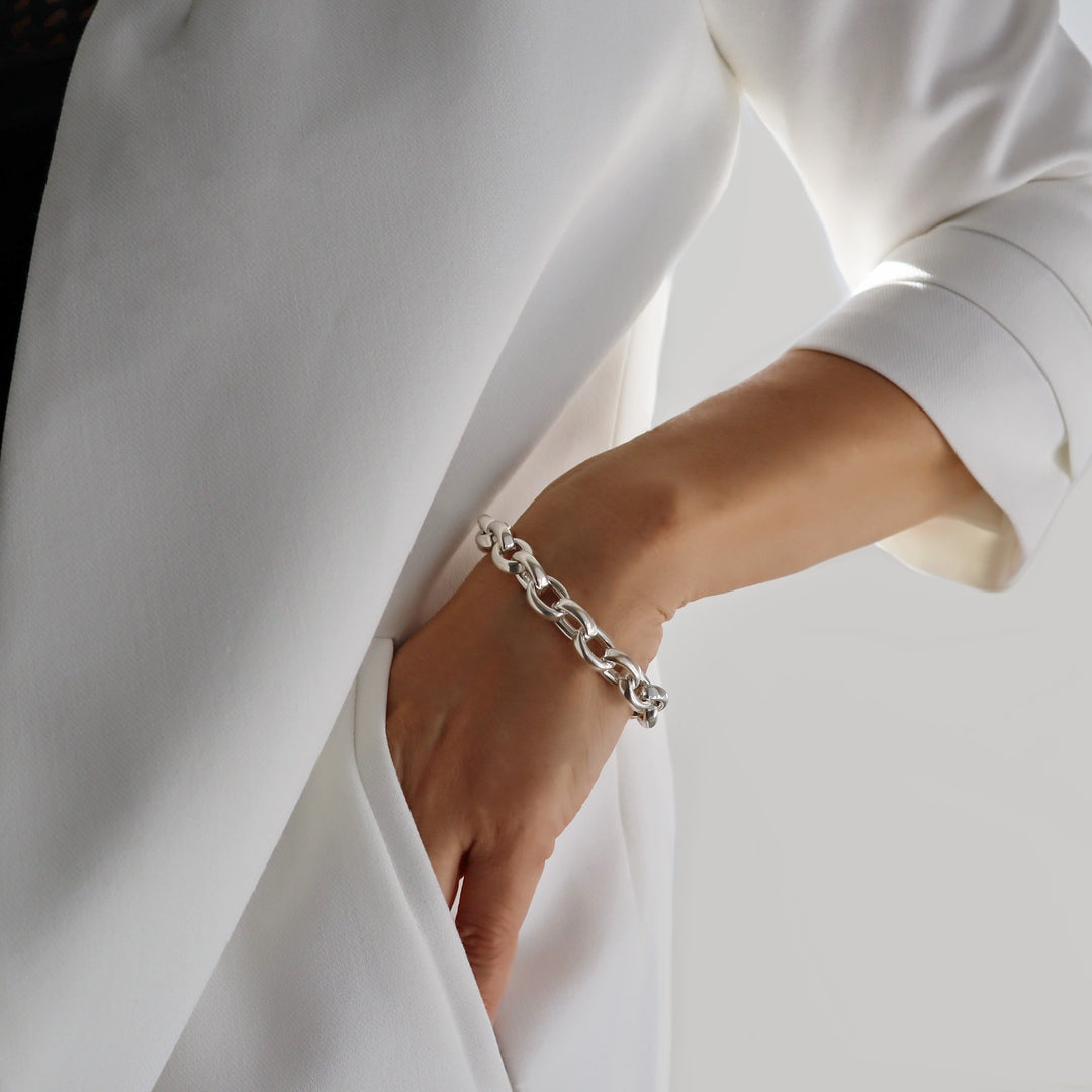 A person wearing a white jacket showcases a chunky sterling silver chain bracelet wrapped around their wrist.