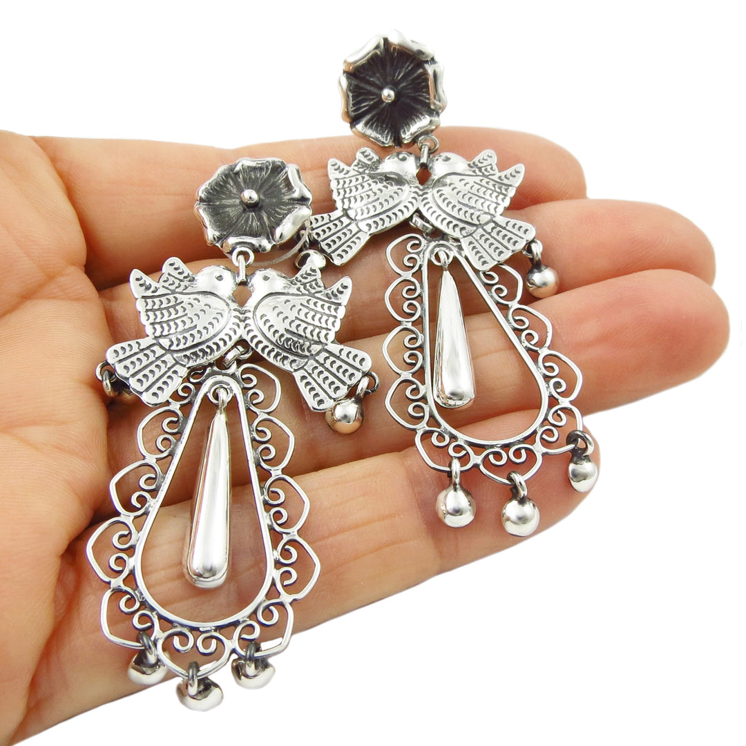 Statement chandelier silver earrings held between fingers