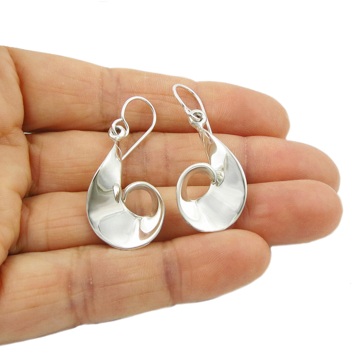 Siral silver earrings held in a person's hand on a white background