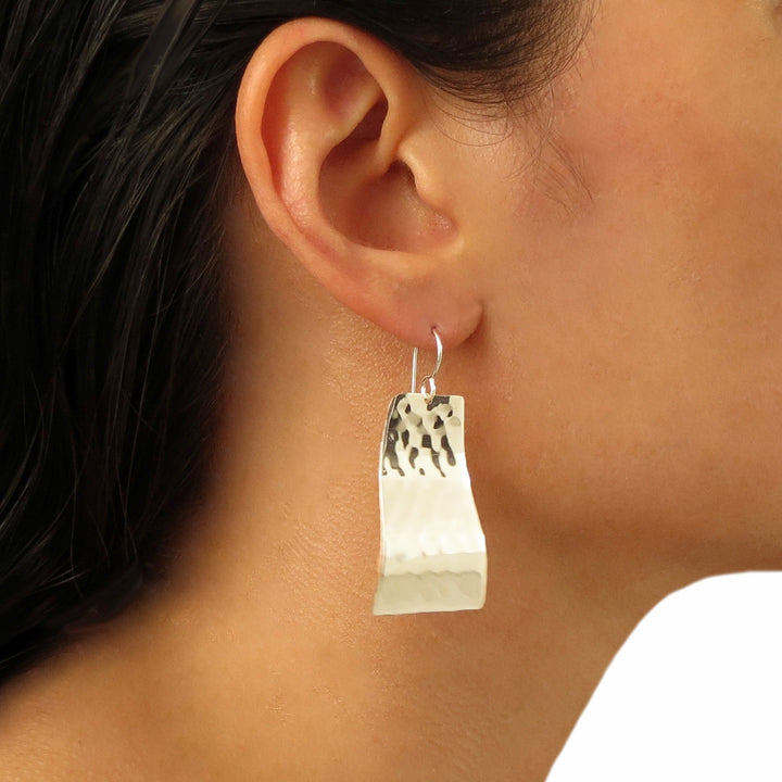 A long curved rectangle earrings with a hammered finish worn by a woman with dark hair.