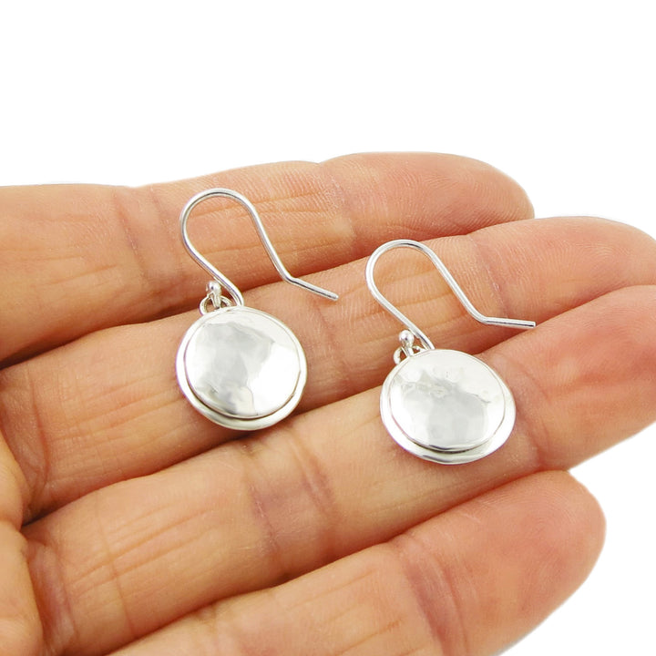 Faceted hammered silver drop earrings held in a person's hand