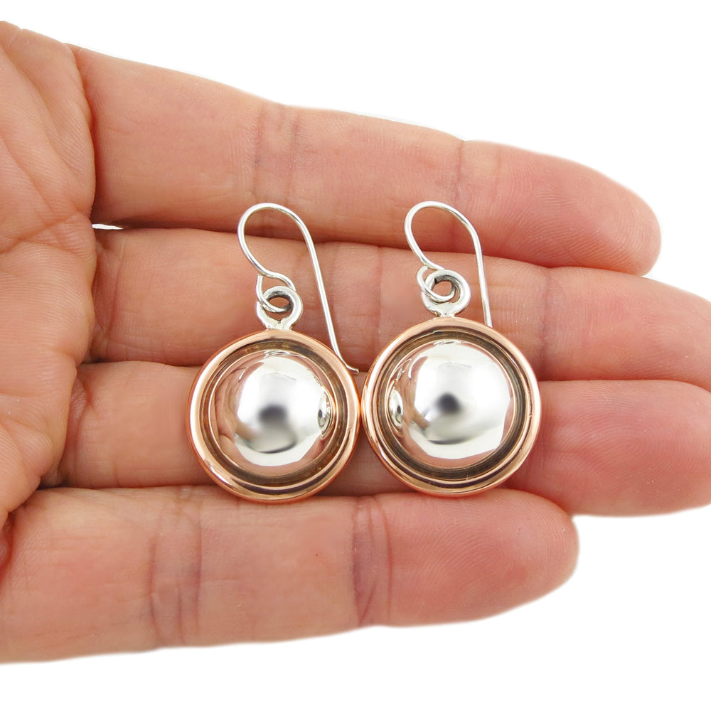 A pair of hoop earrings with copper border and silver center, held in a person's hand.