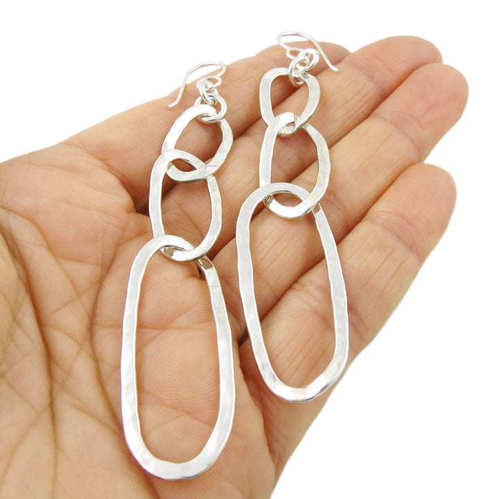 Long dangling curb chain earrings held in a person's hand on a white background