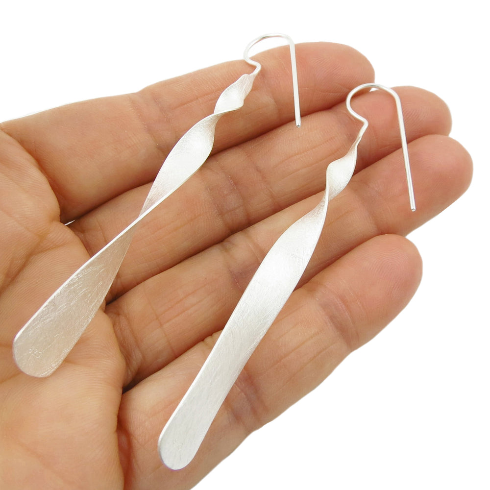 A pair of sterling silver drop earrings with a brushed satin finish, held between fingers.