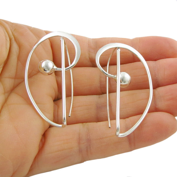 Modern sterling silver spiral drop earrings held in a person's hand.