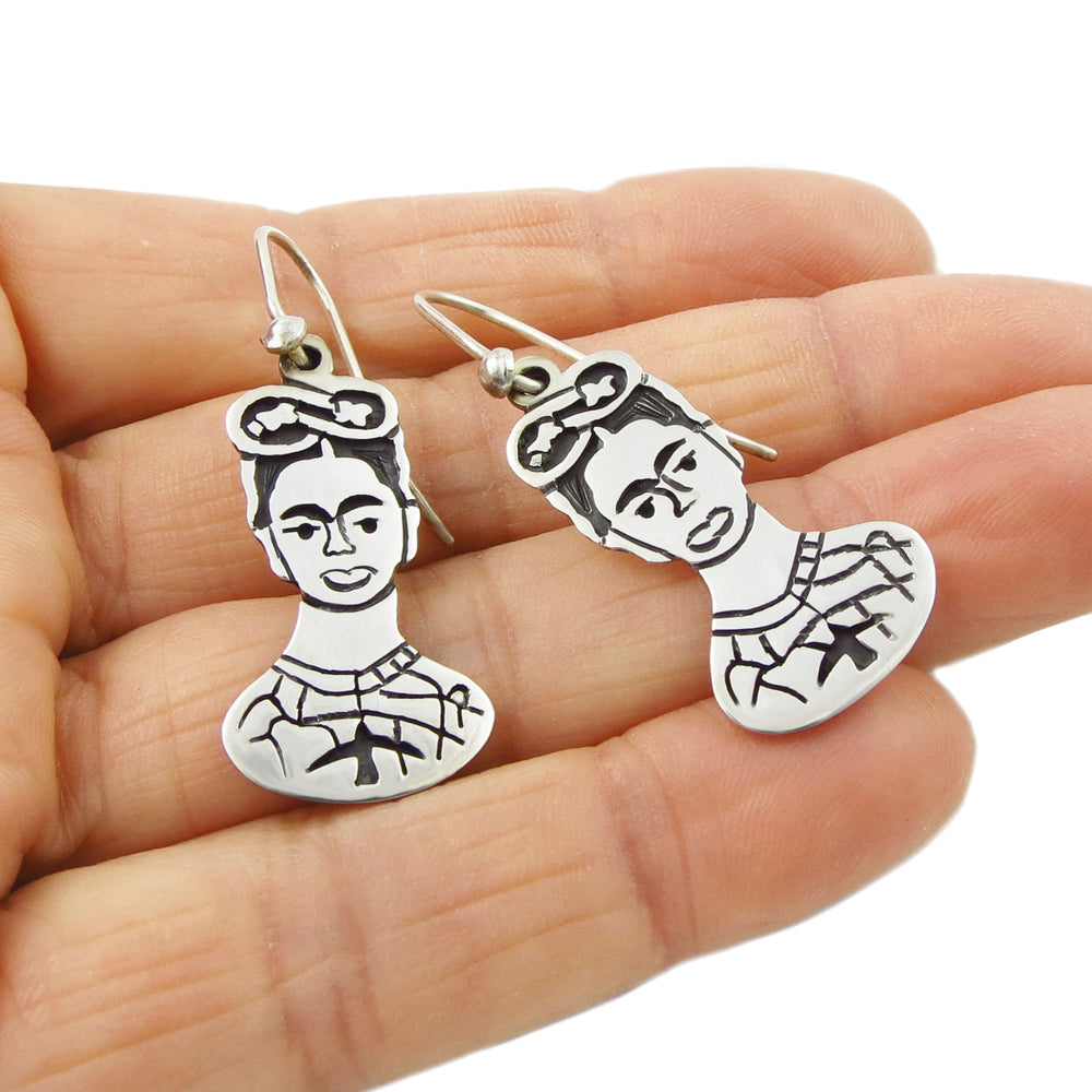 Frida Kahlo silver earrings held in a person's hand.