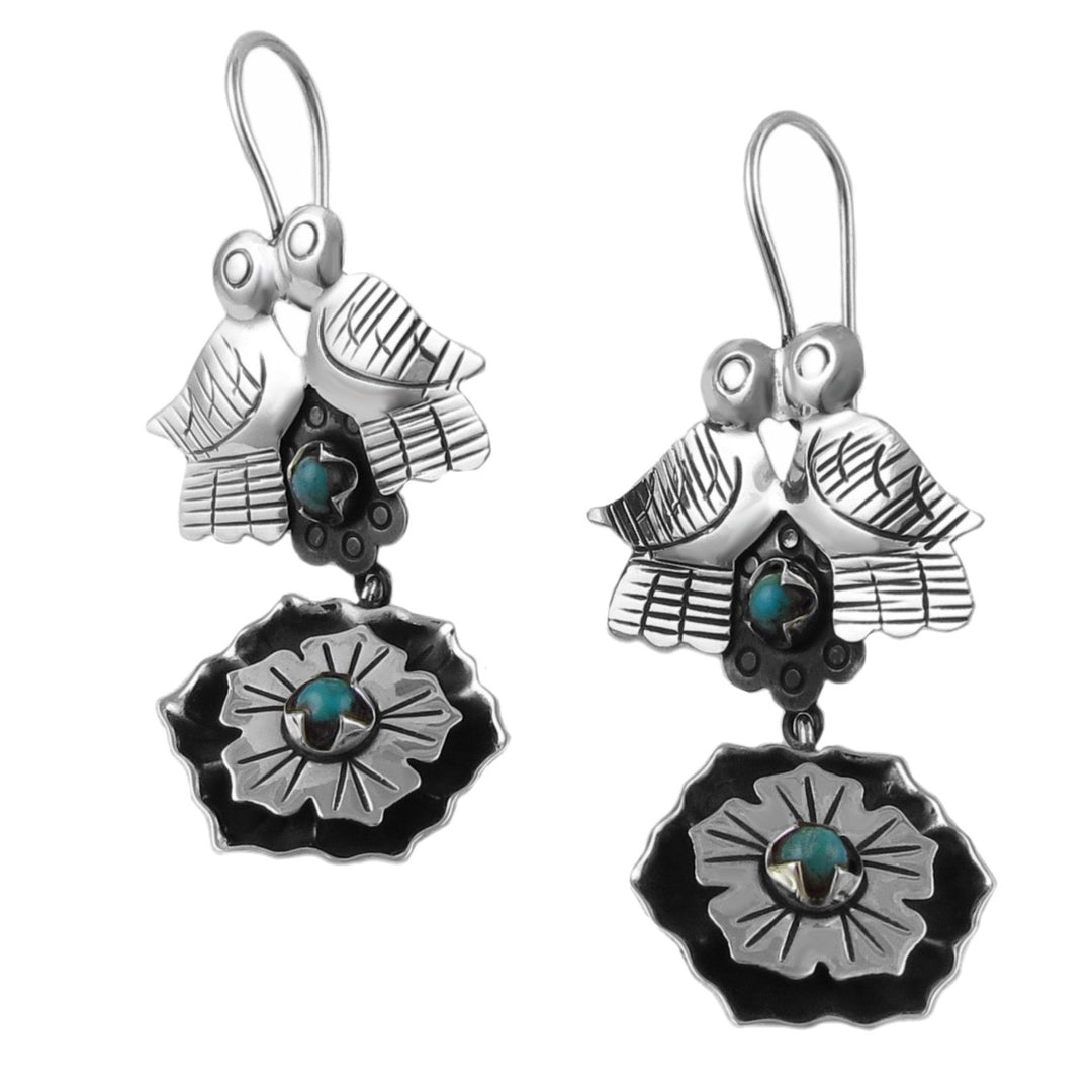 A pair of sterling silver dangling earrings featuring two doves above a turquoise flower, with a geometric pattern on the flower.