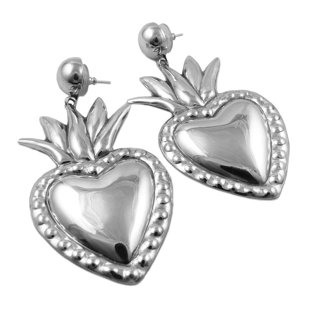 A pair of sterling silver heart-shaped earrings with a high polish finish and intricate detailing, hanging from large demi-beads.