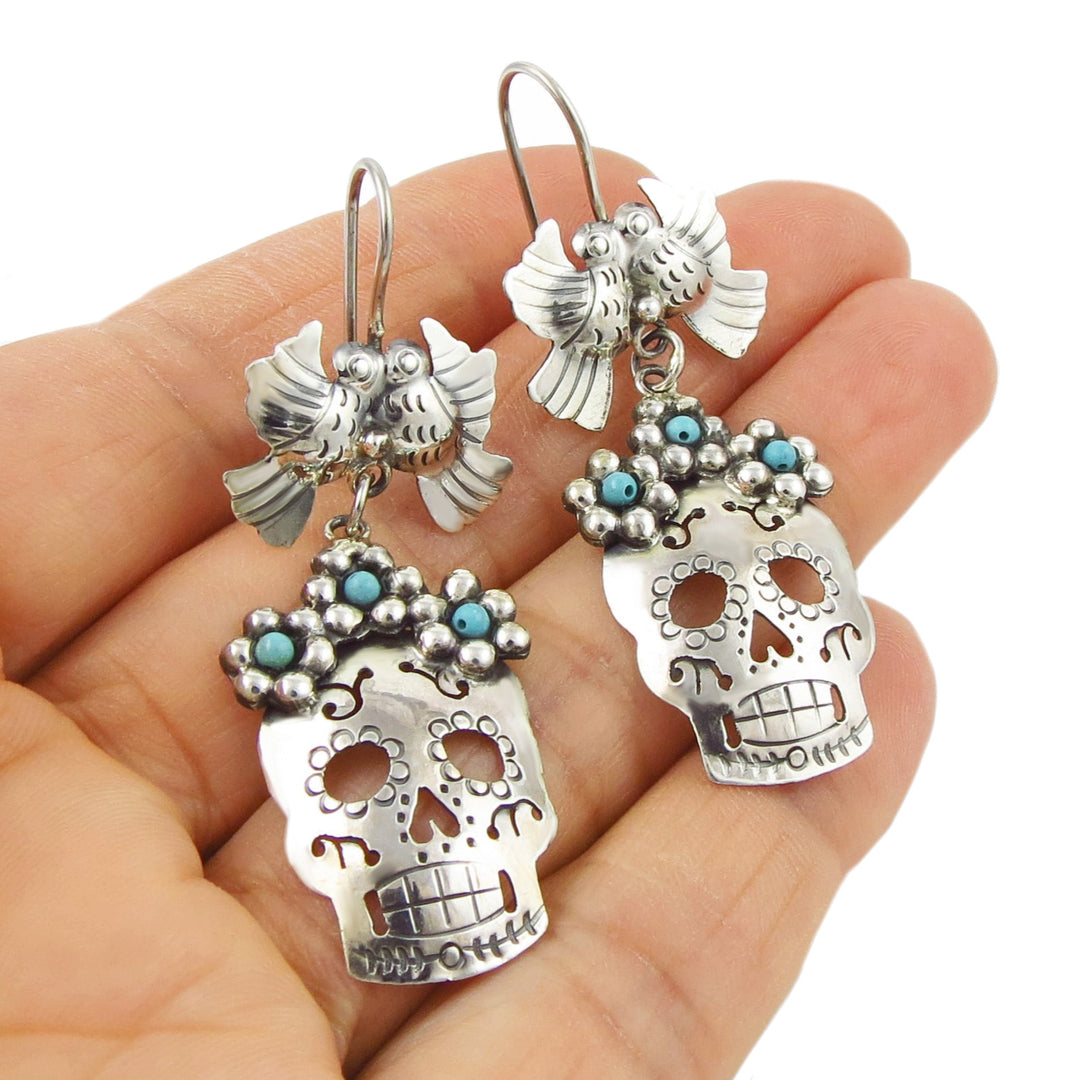 Sterling silver day of the dead sugar skull earrings held in a person's hand.