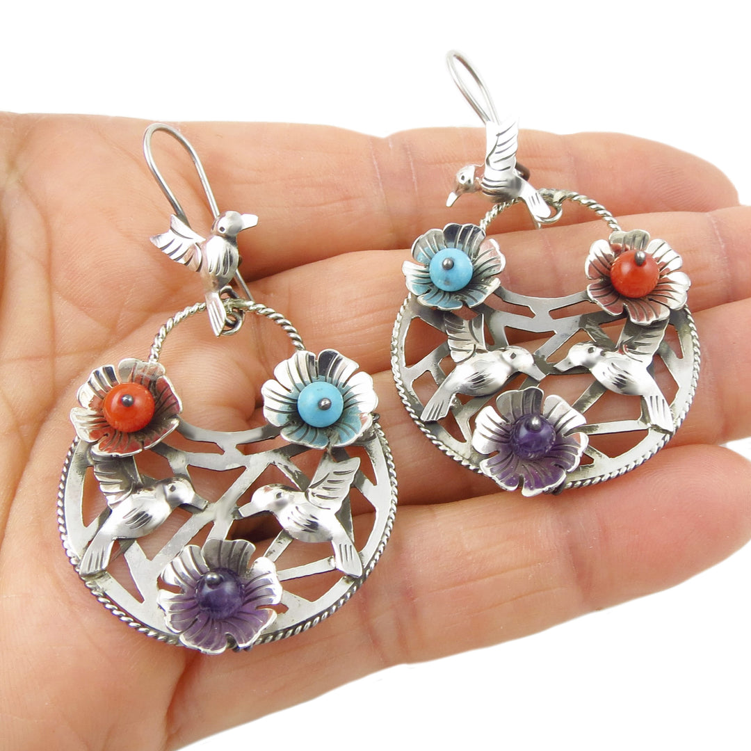 A pair of sterling silver drop earrings featuring lovebird motifs with colorful flower accents in turquoise, amethyst, and coral shades.