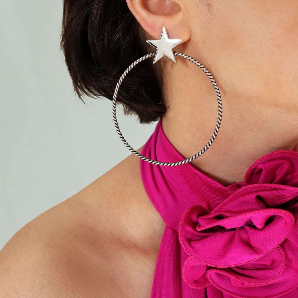A close-up image of a person wearing a silver star-shaped hoop earring with a polished finish.