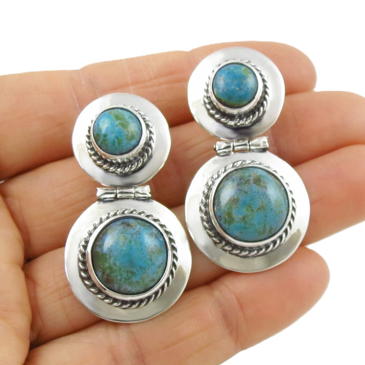 Sterling silver earrings with turquoise gemstone held in a person's hand.