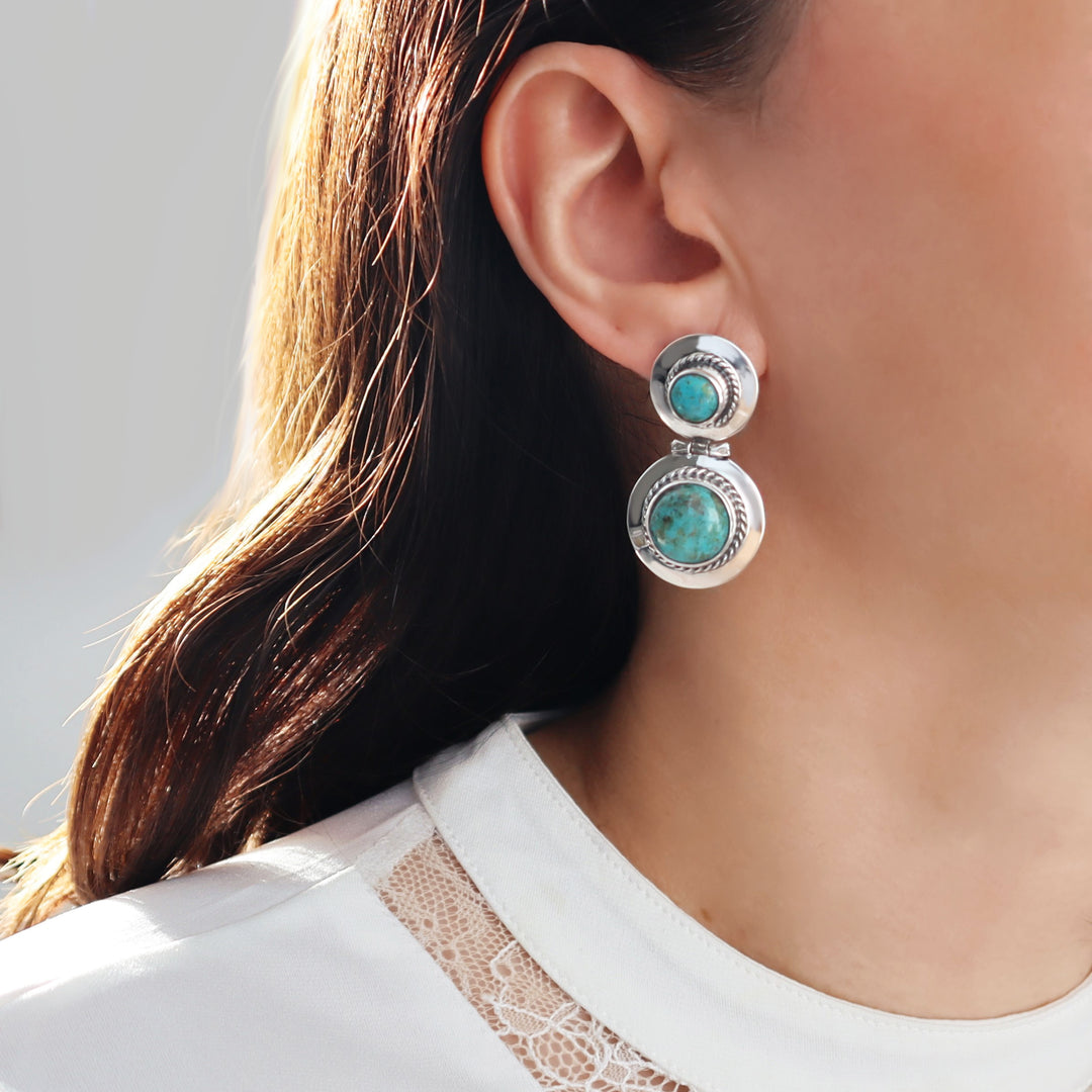 A person wearing sterling silver drop earrings with turquoise gemstones.