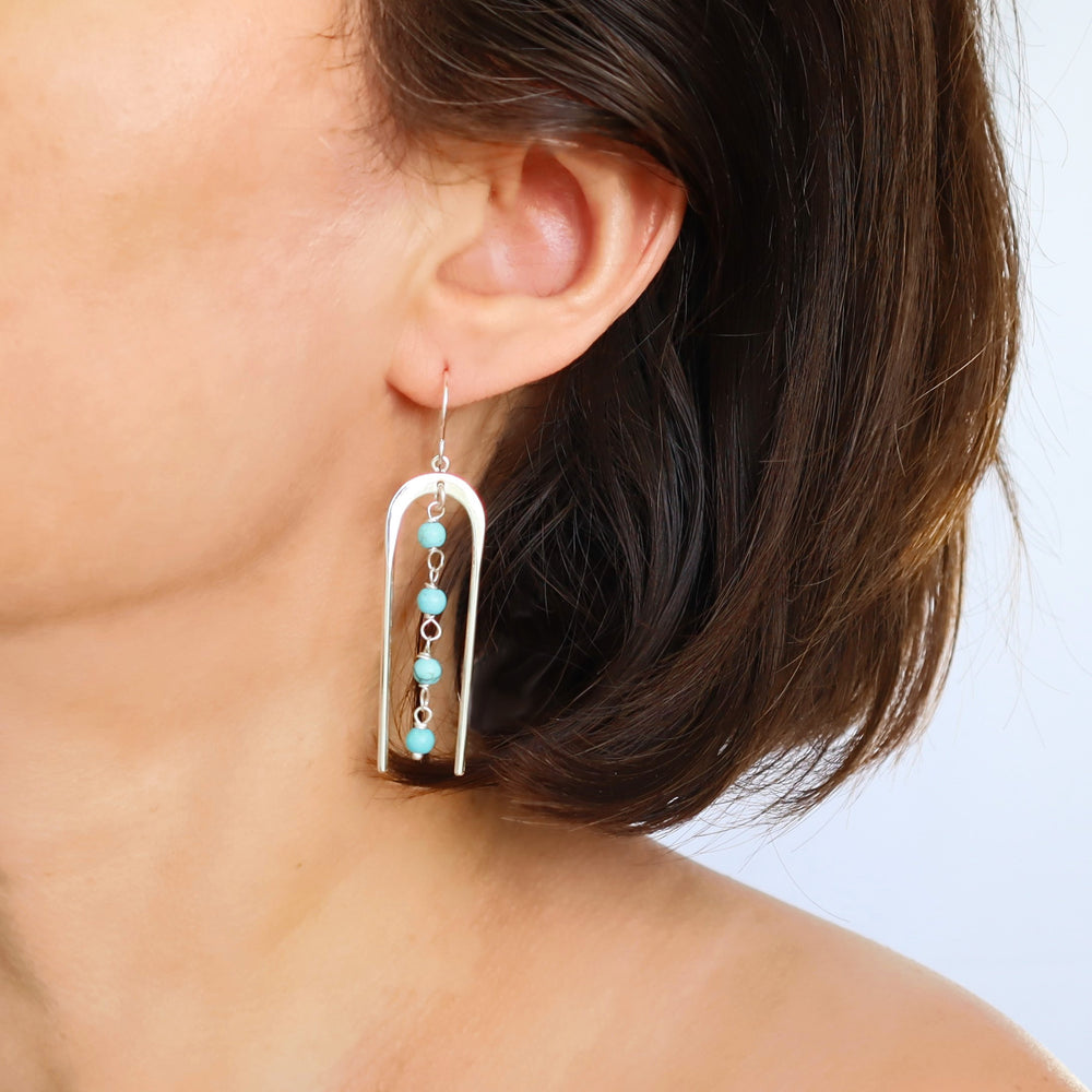 A photo showing a pair of long dangling turquoise bead sterling silver earrings worn by a woman