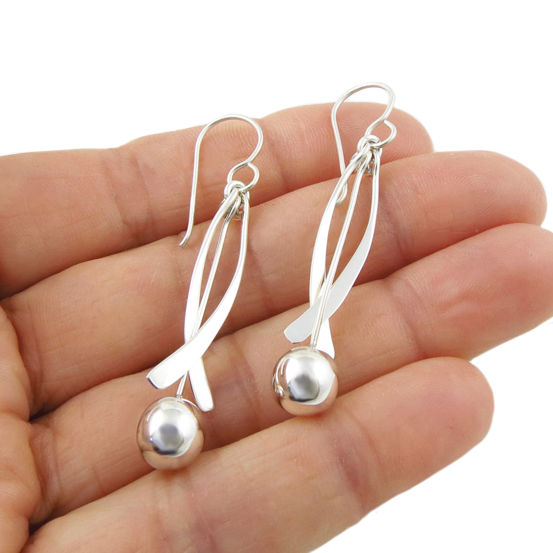 Long 925 silver earrings with round ball beads held in a hand on a white background