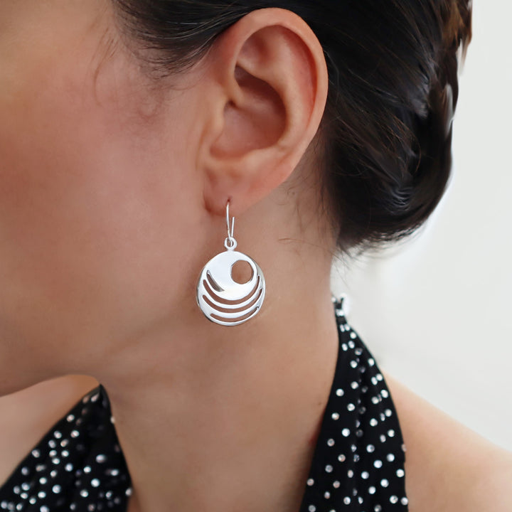 A sterling silver circle earring worn by a woman with a sparkly halter top