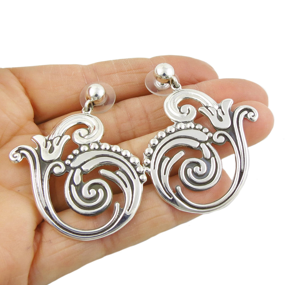 Taxco design ornate flower and vine silver earrings held in a person's hand