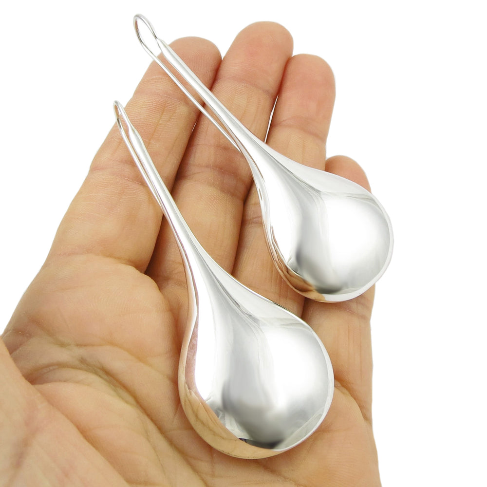 A pair of large sterling silver teardrop earrings held in a hand, with a highly polished finish.