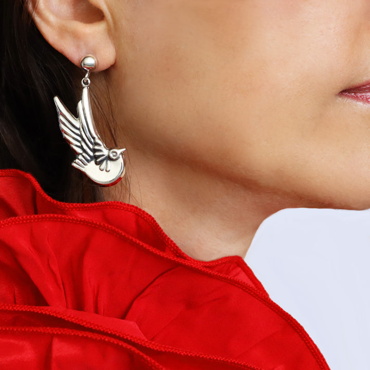 Taxco design silver lovebird earring worn by a woman with a red blouse