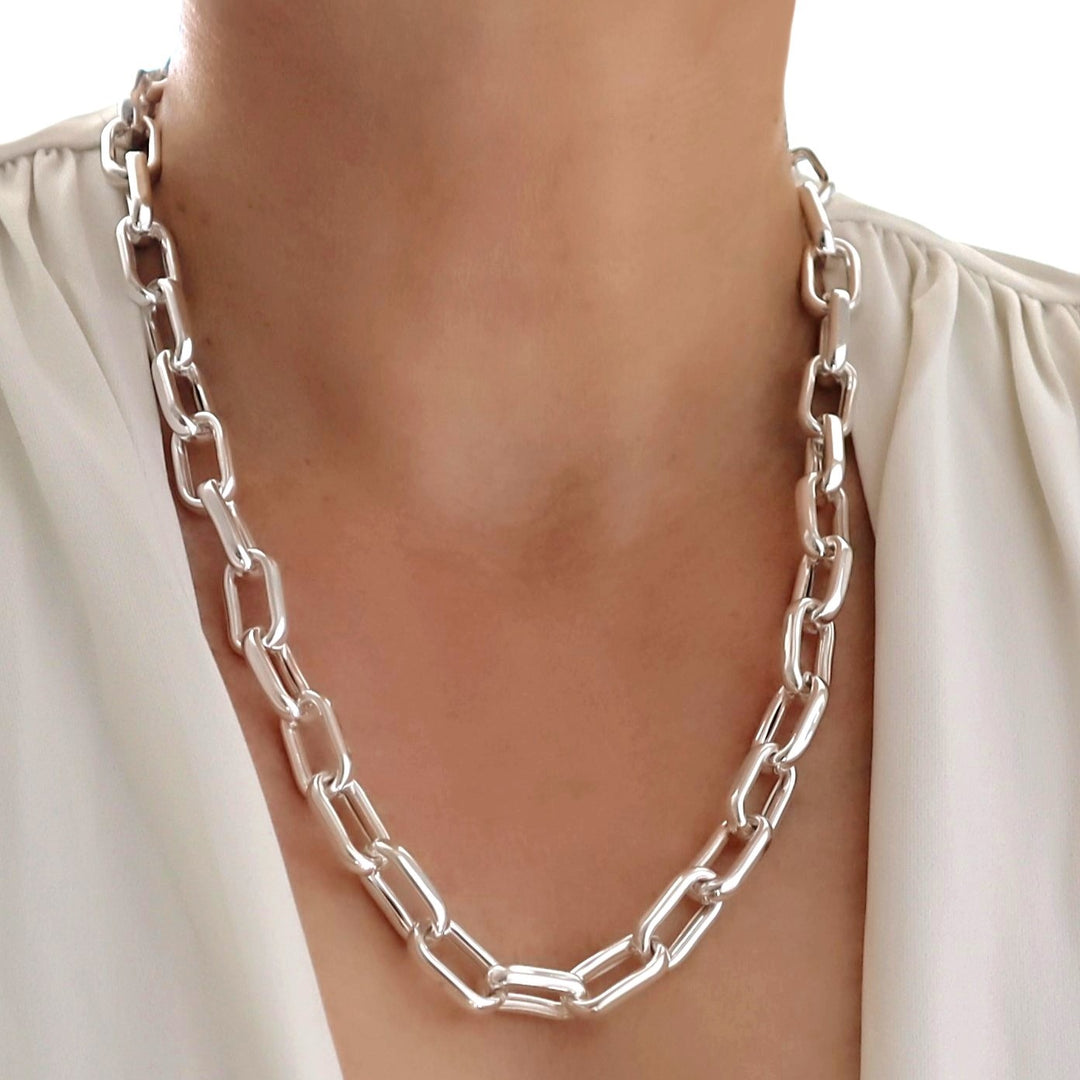 A person wearing a silver rectangular chunky chain necklace.