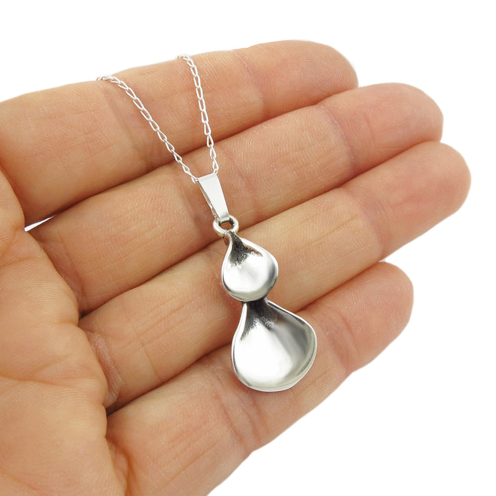 Silver flower petal pendant necklace held in a hand on a white background