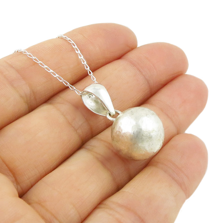 Silver necklace with a round ball bead pendant held in a hand on a white background