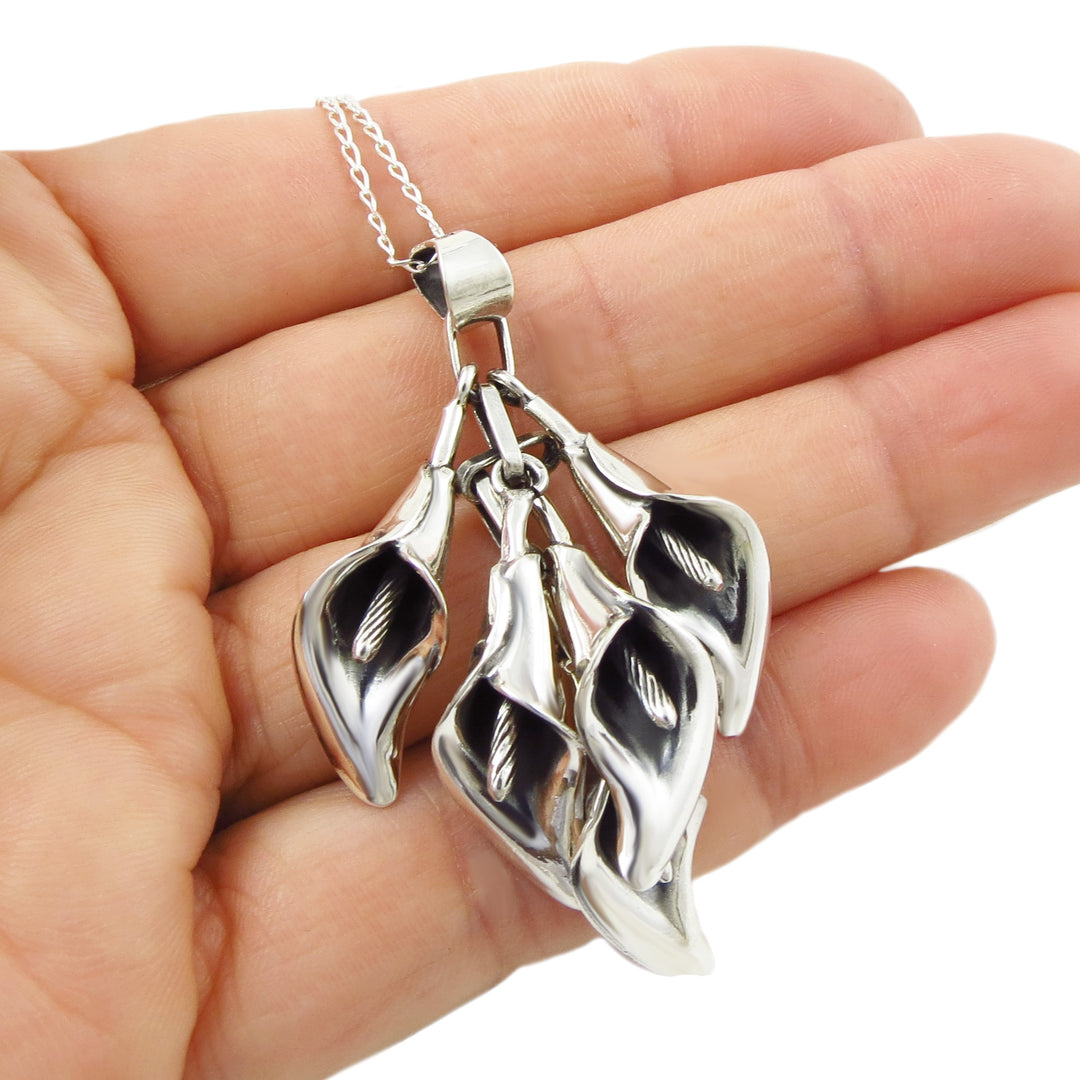 Silver calla lily pendant necklace held in a hand against a white background