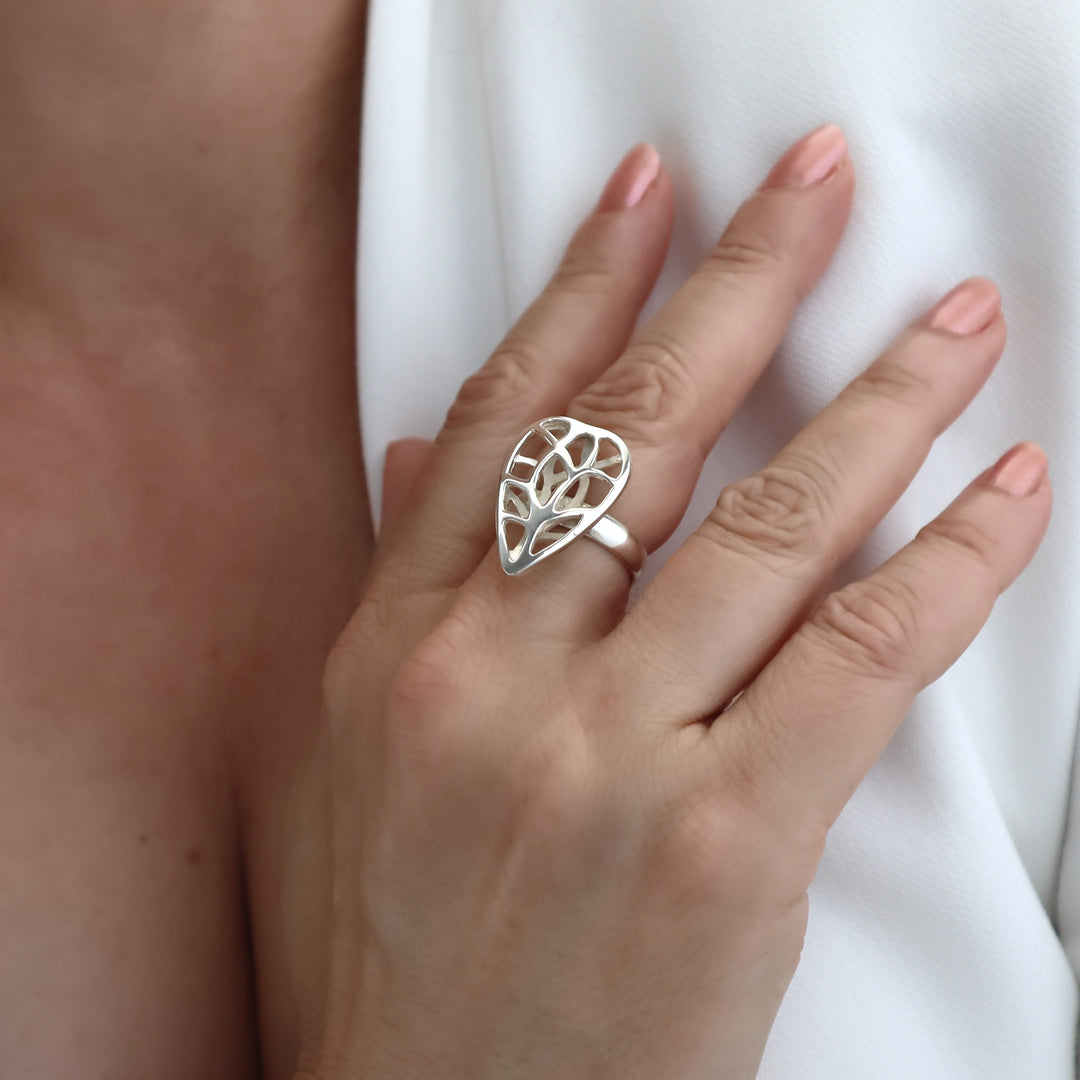 Silver ring with leaf design on a woman's hand against a white background