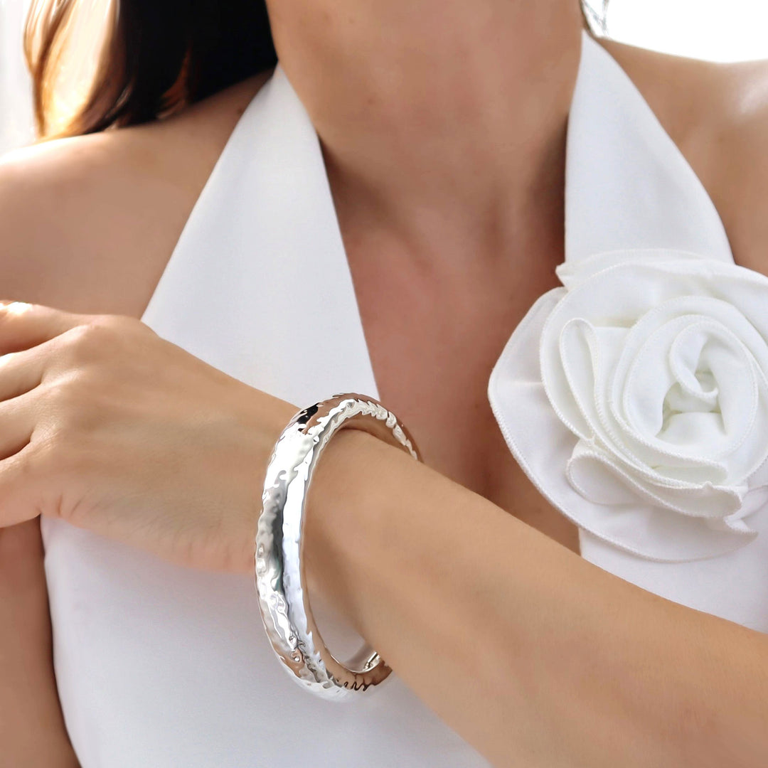 A woman wearing a white dress and a silver, hand-hammered finish, chunky bangle  on their wrist.