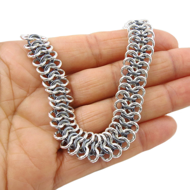 Silver chain bracelet with polished and blackened rings held in a person's hand.