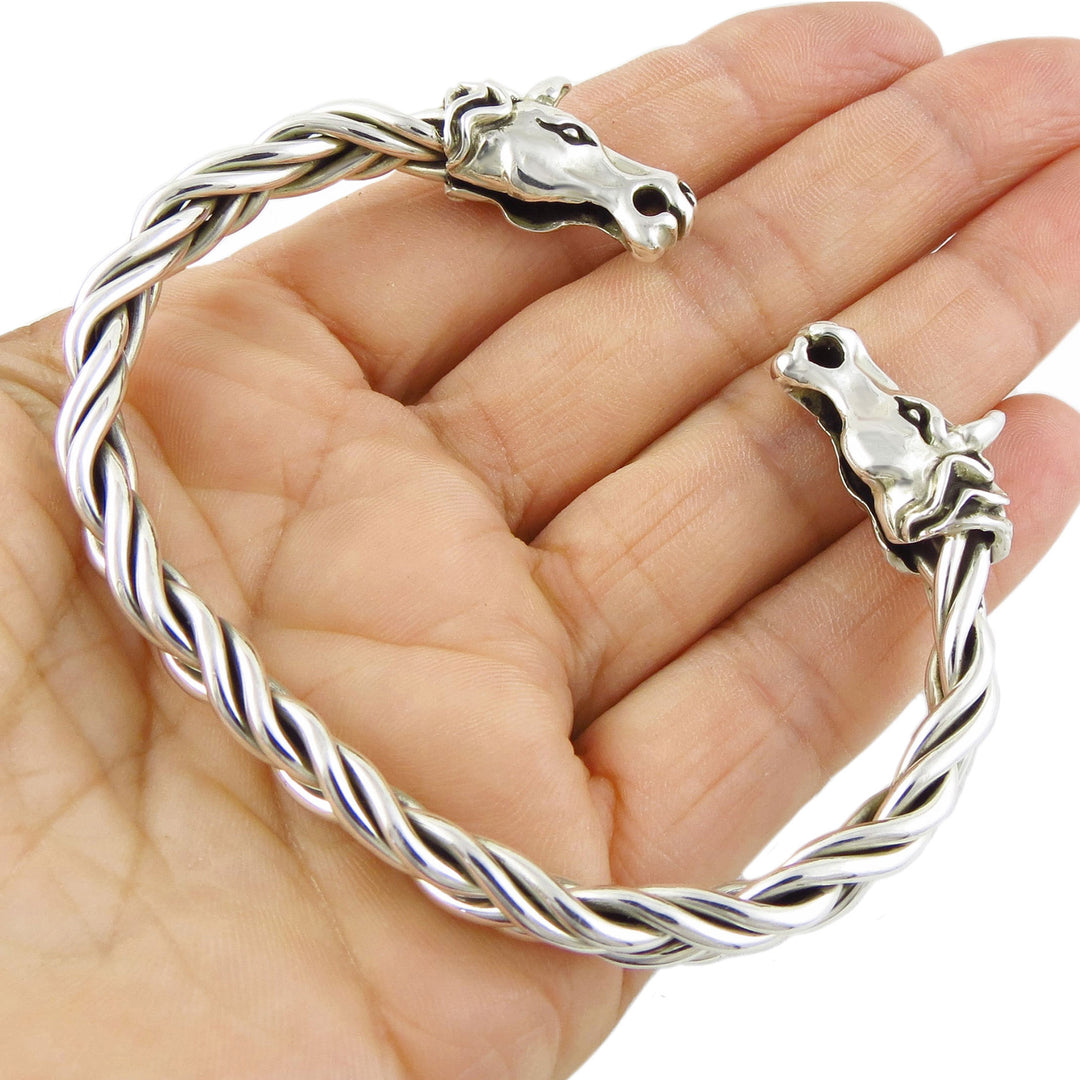 A larger twisted sterling silver bracelet cuff with horse heads held in a person's hand.