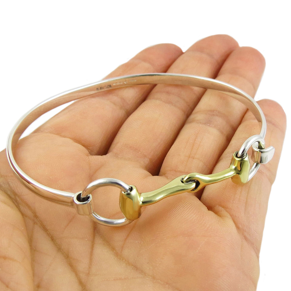 A two tone silver bracelet with a horsebit accent being held in a hand on a white background