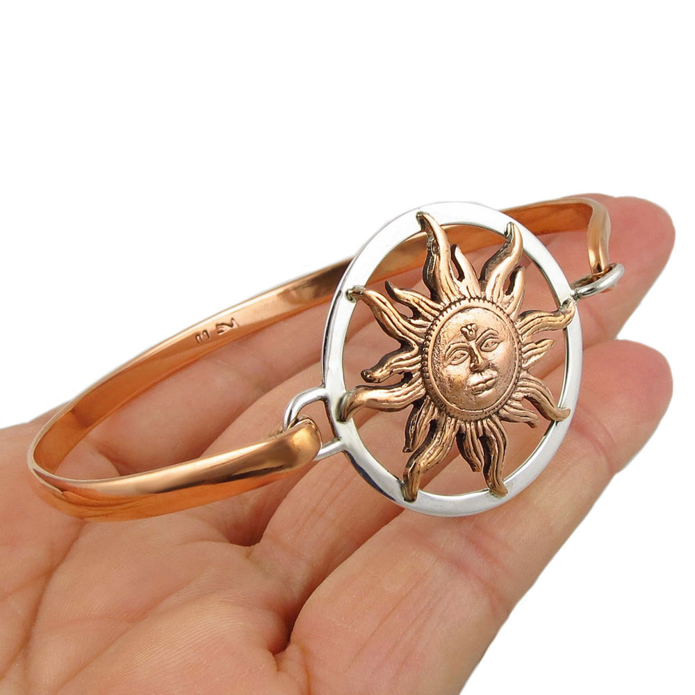 Copper and silver bracelet with a sun motif at the centre held in a person's hand.