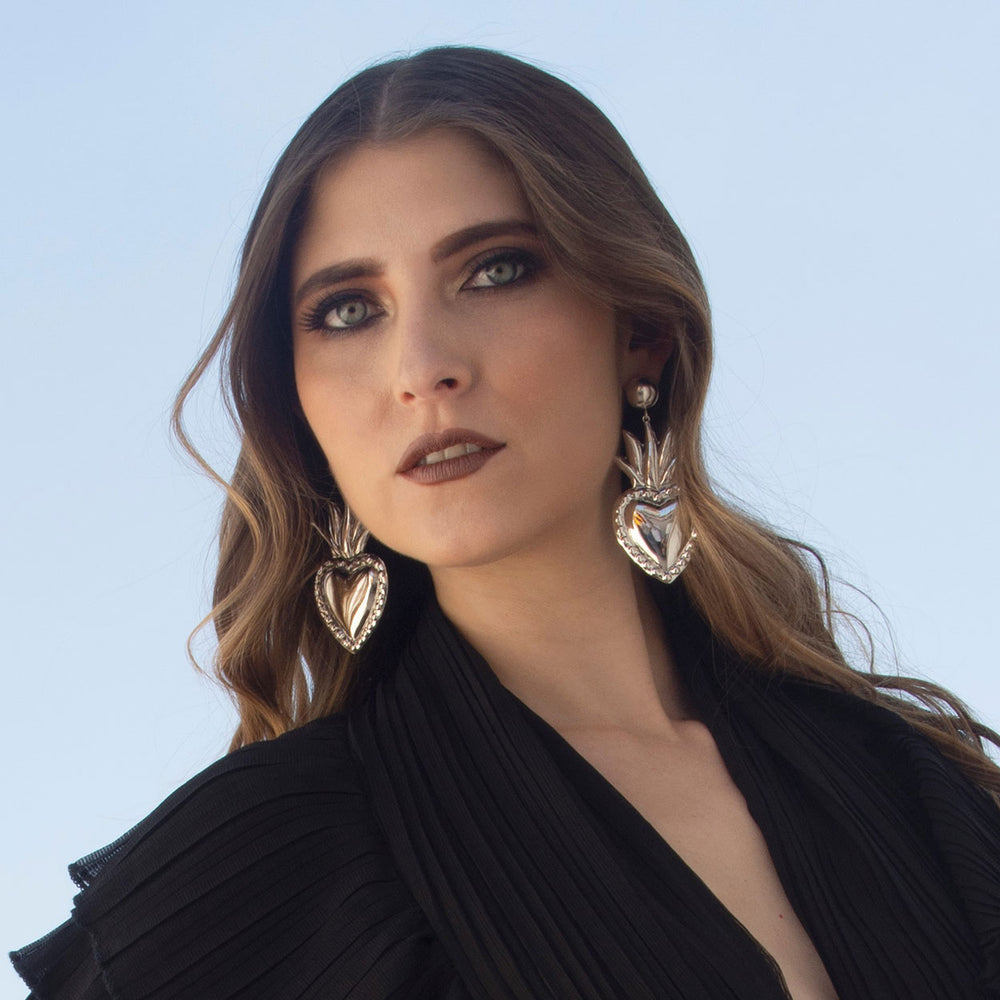 Large polished heart drop earrings in sterling silver worn by a woman with a black blouse.