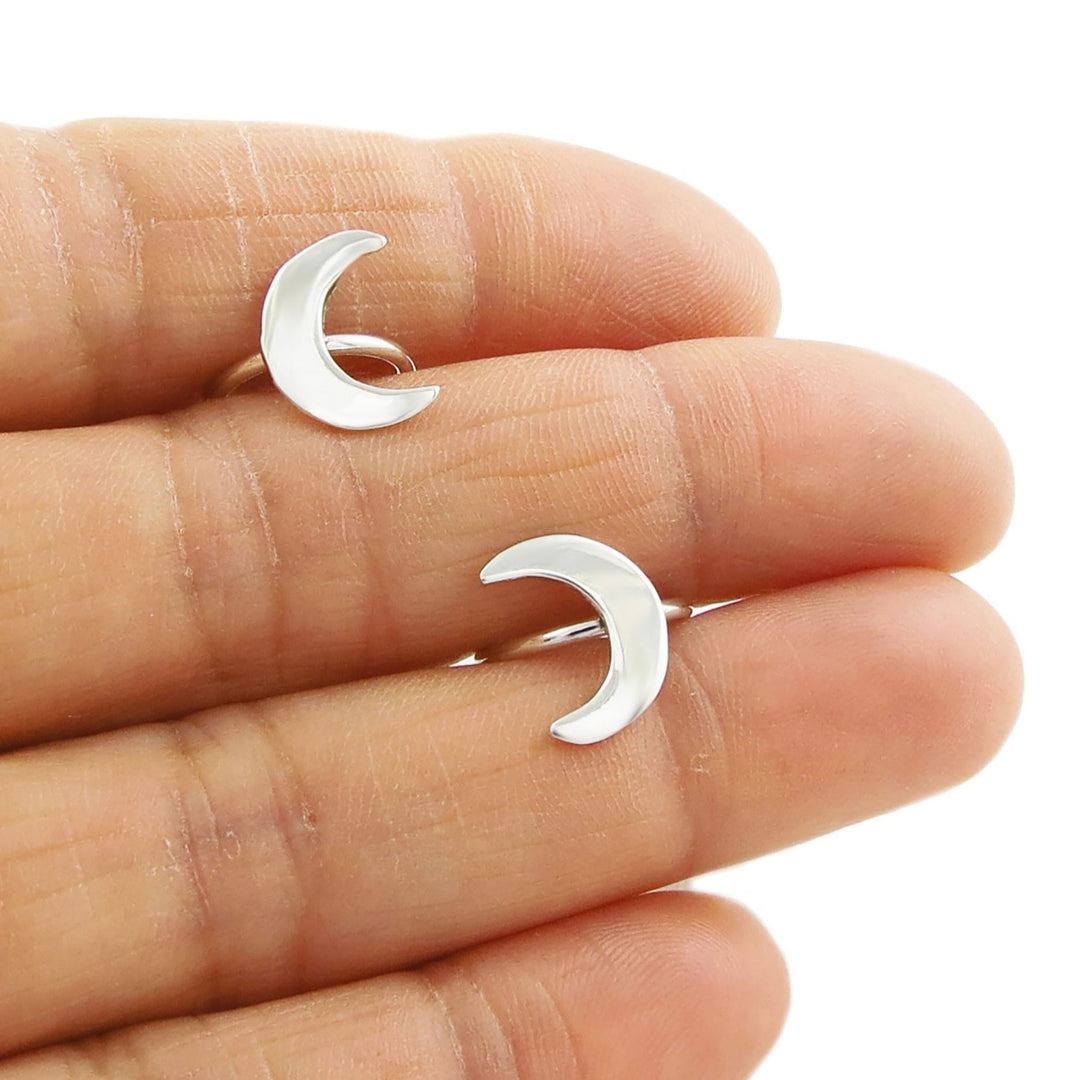 A person's hand holding a silver crescent moon ear cuffs.