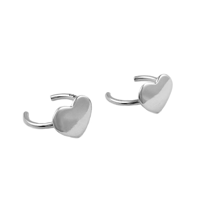 A pair of sterling silver heart-shaped ear cuffs laid on a white surface.