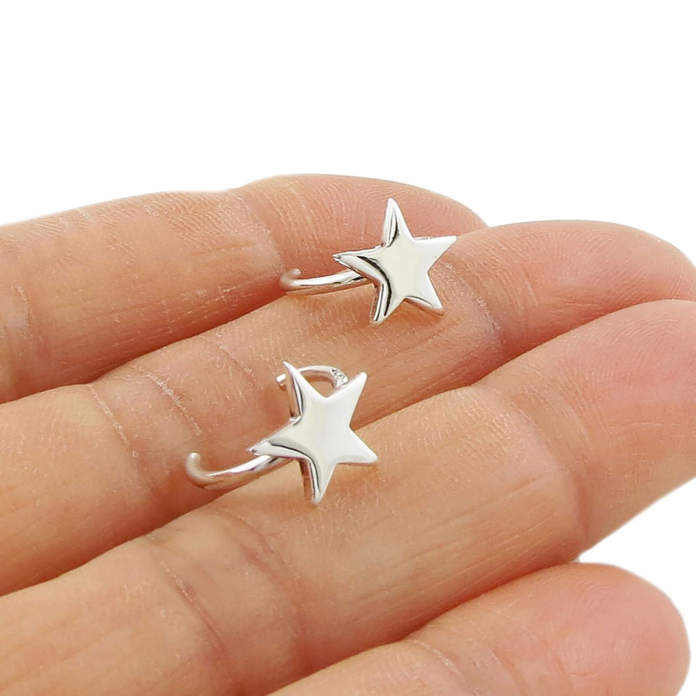 A pair of silver ear cuff earrings shaped like stars, displayed on a person's hand.