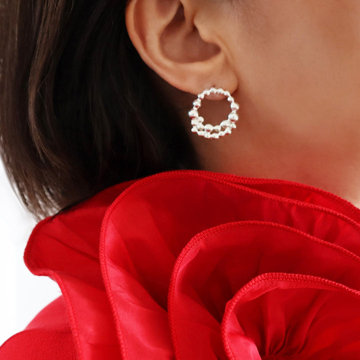 Silver bubble hoop earrings worn by a woman with a ruffled red blouse
