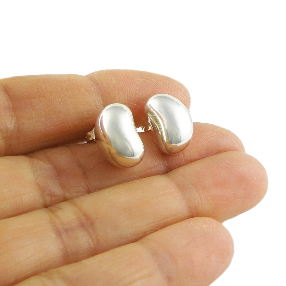 A pair of silver bean-shaped silver stud earrings held in a person's hand.