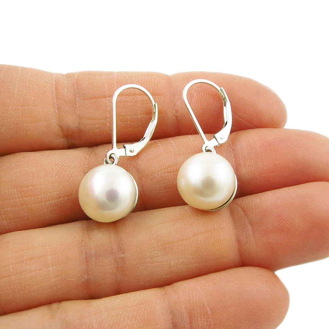 A pair of freshwater pearl and 925 silver earrings with French hooks held in a person's hand.