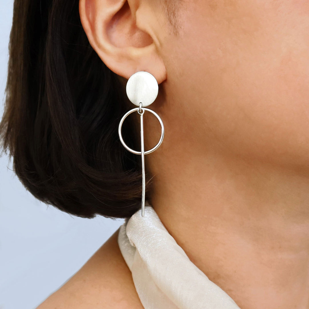Long dangling silver earrings worn by a woman with a cream halter top